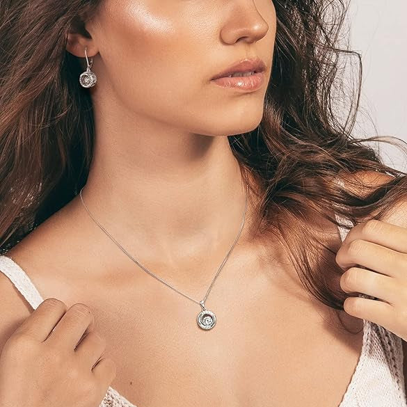 Close-up of a woman wearing a white top with thin straps, focusing on her neckline and necklace, with matching earring.